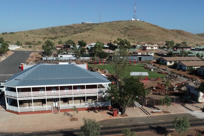 Aerial view of two-storey building with white verandahs in a town with a hill in the background.