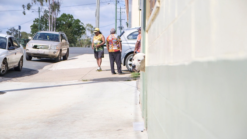 People meet on the street as a dog watches from the doorway of the police station