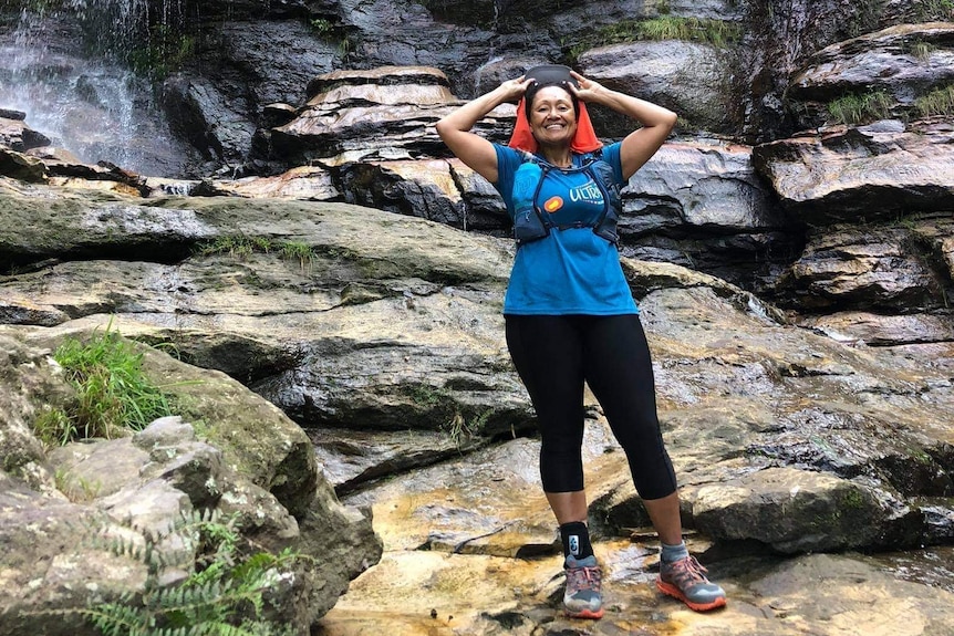 A woman stands in front of a waterfall with running gear on.