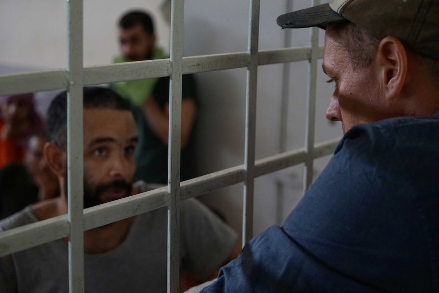 A warden talks to a prisoner through the bars of his cell.