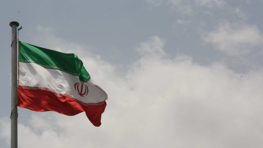 A hoisted Iranian flag flutters against a cloudy sky.