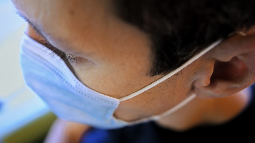 The side of a man's head showing his face mask string wrapped around his ear