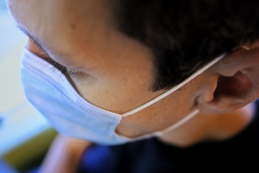 The side of a man's head showing his face mask string wrapped around his ear