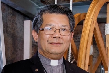 A headshot of a Vietnamese man wearing a Catholic priest's collar. 