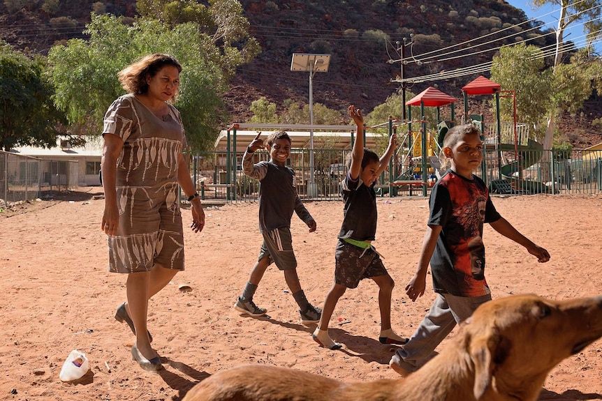 Leanne Liddle walks with three children in Areyonga in front of a playground.
