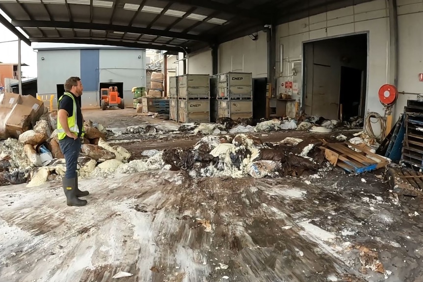 man wearing high vis surrounded by piles of muddied ice cream and product outside a factory door