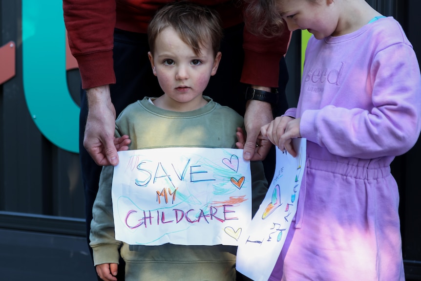 A young boy holds a sign that says Save My Childcare.