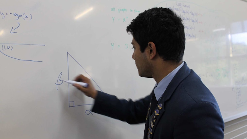 A 17-year-old boy writing on a white board. He's wearing a navy blue school uniform.