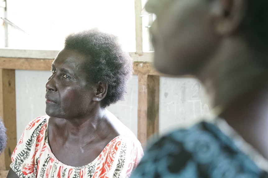 Two women sit and listen to a Sivuna village meeting.