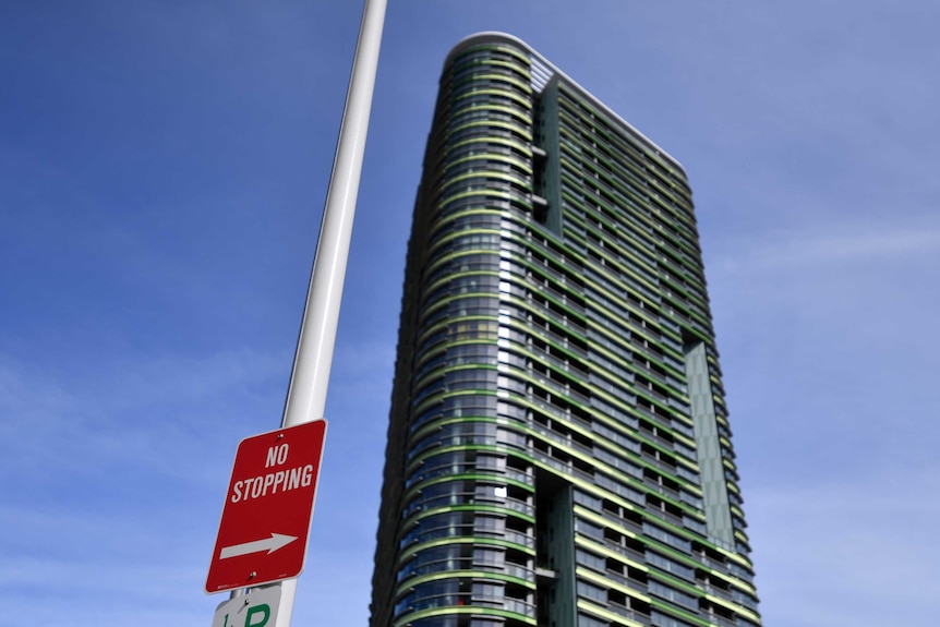 A sign that says 'no stopping' in the foreground in front of a tall apartment building, Opal Tower.
