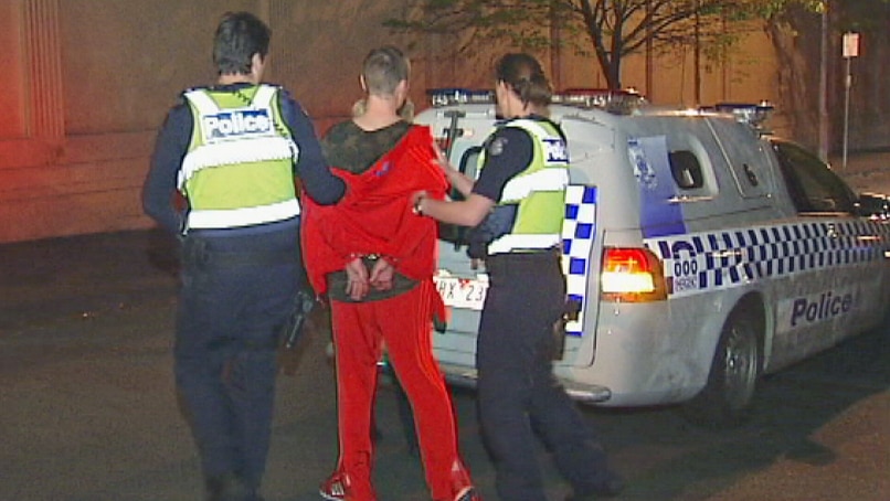 A handcuffed man is led to a police wagon outside the Melbourne ABC building