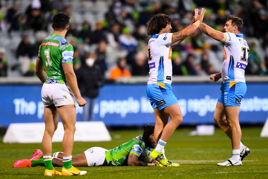 Two Gold Coast NRL players high five each other as Raiders opponents look on.