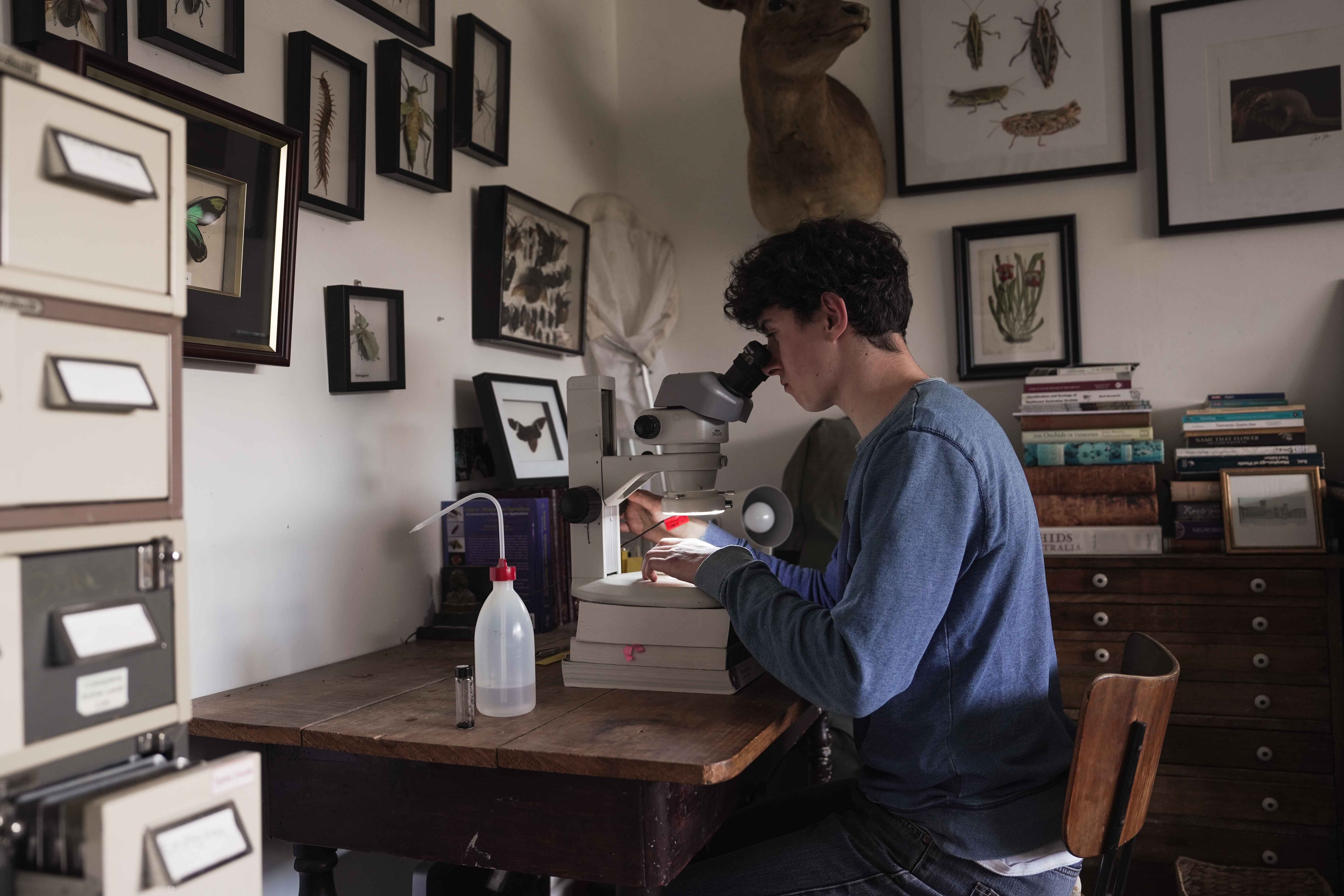 A man sits at his desk using a microscope.