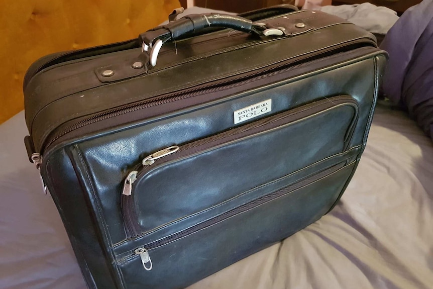 A black travel case sitting on a bed