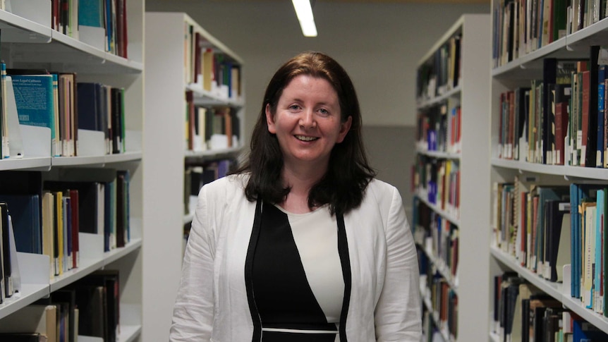 Dr Margaret McGrath standing between two rows of books at the library.