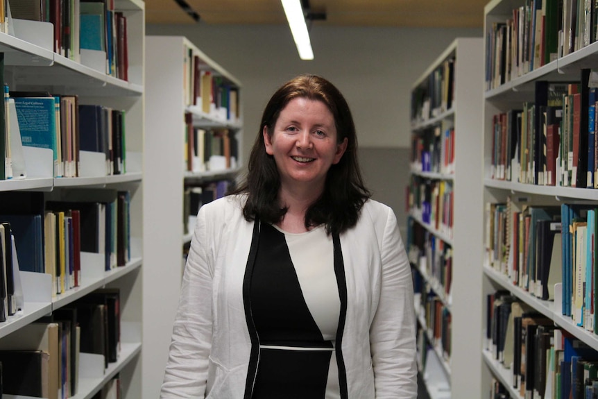 Dr Margaret McGrath standing between two rows of books at the library.