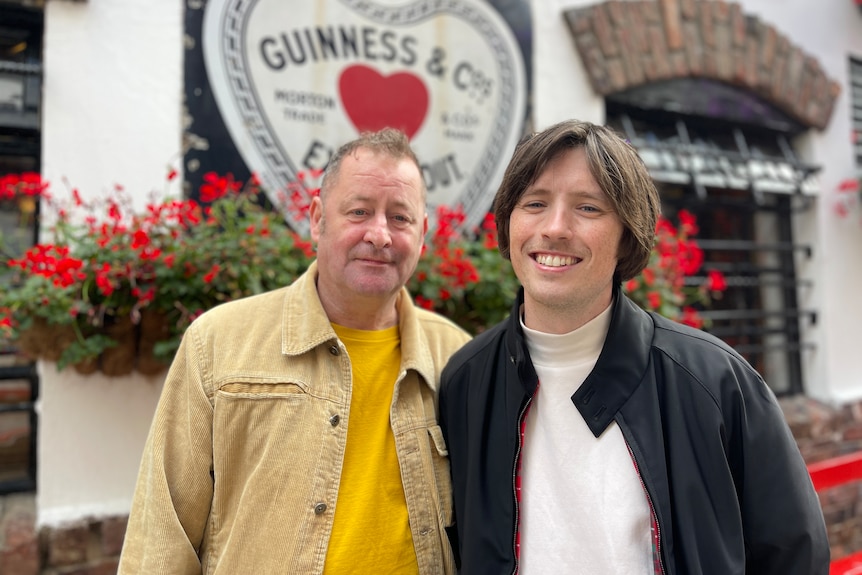 Two men, one older than the other, pose in front of a Guinness sign on a pub in Belfast.