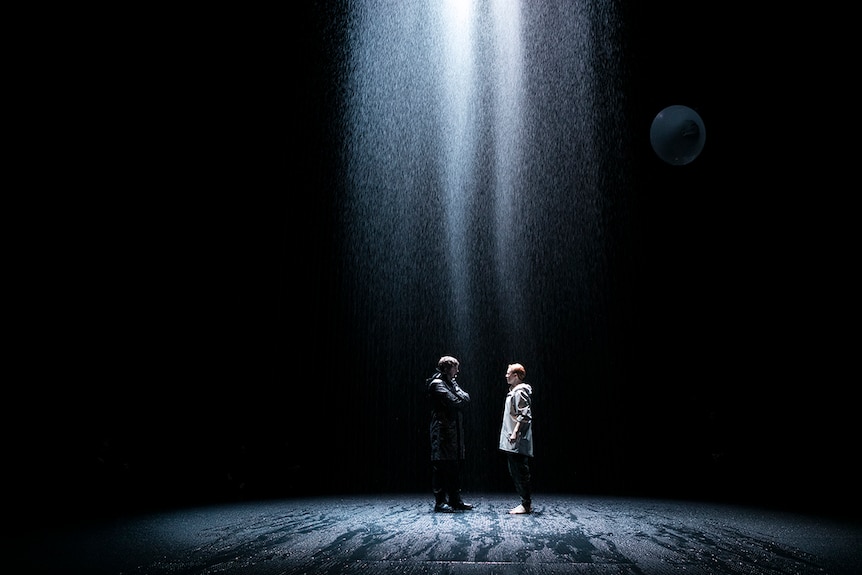 Colour production still of two characters standing face to face in the rain on stage in 2018 theatre production Saint Joan.