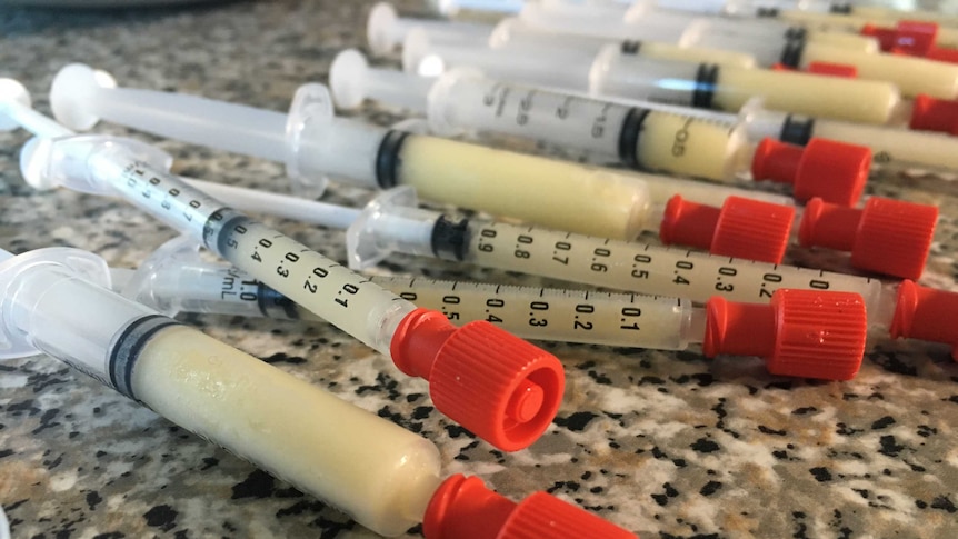 Small syringes filled with frozen breastmilk are scattered across a bench top.