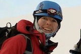 A woman in heavy cold-weather hiking gear stands on a mountain.