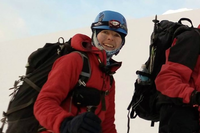 A woman in heavy cold-weather hiking gear stands on a mountain.