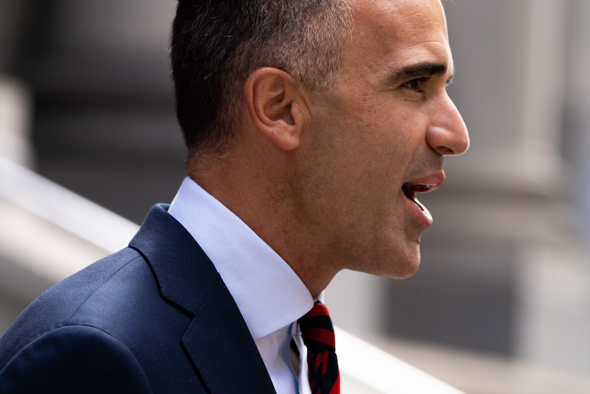 A man wearing a navy suit and red tie looking to the right of camera