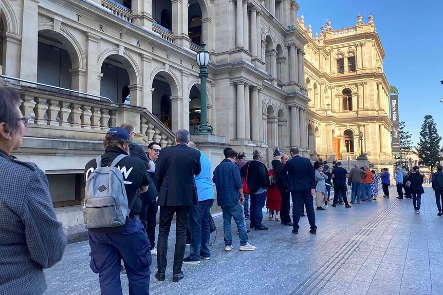 A queue of people standing outside an old stone building in the Brisbane CBD