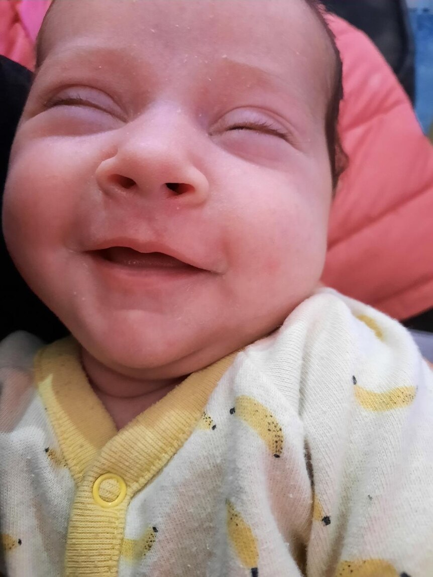 A smiling baby with her eyes closed.
