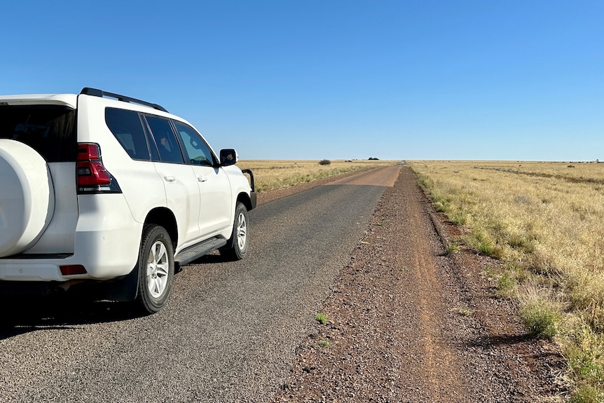 White 4WD driving on gravel road with blue sky above. 