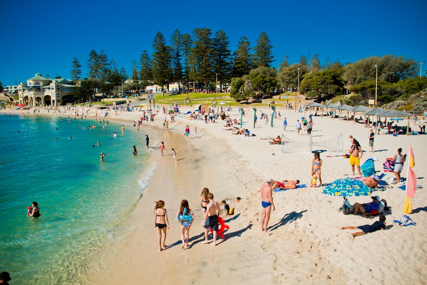 A white stretch of beach curves around turquoise waters with bathers dotting the sand.