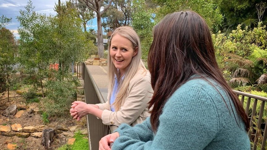 Two women speak to each other while leaning over a railing