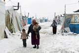 A Syrian refugee holds a barefoot child as she walks with a girl through snow at a refugee camp in Lebanon's Bekaa Valley.