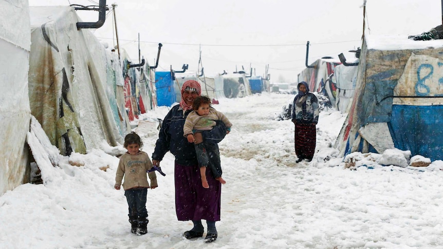 A Syrian refugee holds a barefoot child as she walks with a girl through snow at a refugee camp in Lebanon's Bekaa Valley.
