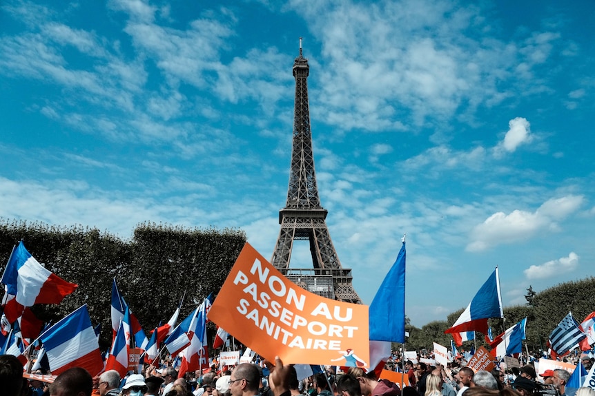 Protesters hold French flags and signs in front of the Eiffel Tower.