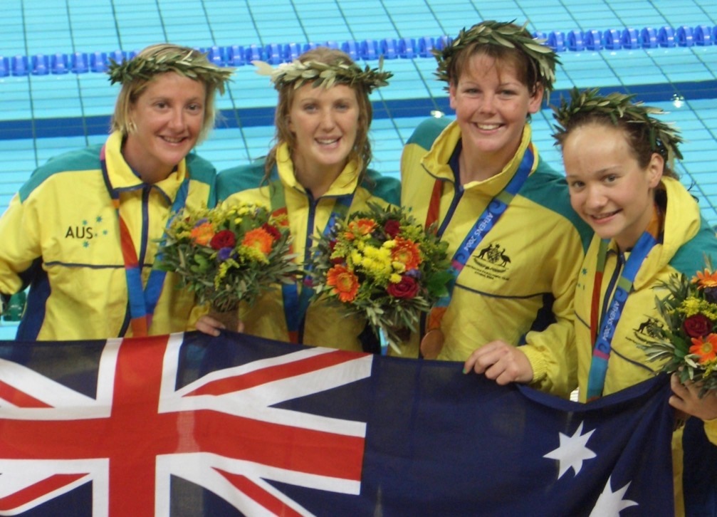 Four swimmers wearing their bronze medals and holding an Australian flag are smiling