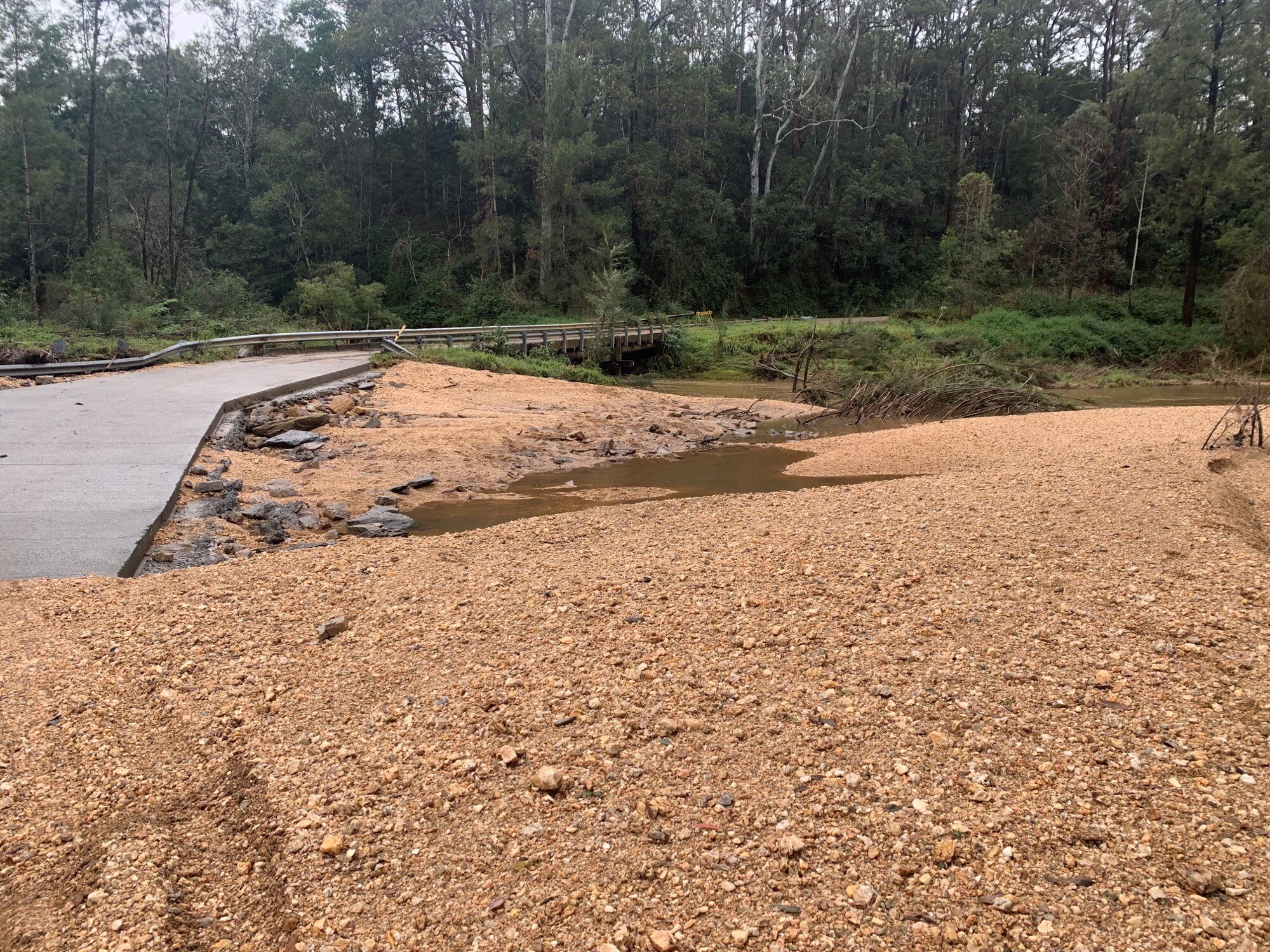road with gravel partially damaged with puddles of water surrounded by trees