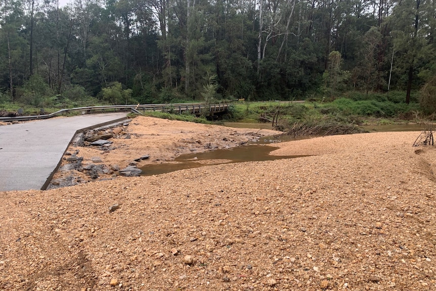 road with gravel partially damaged with puddles of water surrounded by trees