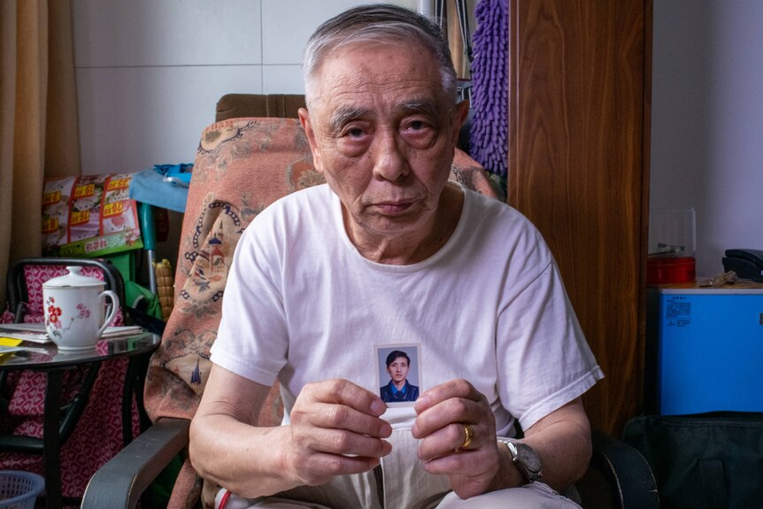An elderly Chinese man holds a photo of a younger Chinese man.