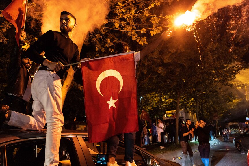 A young man holds a Turkish flag on a car at night