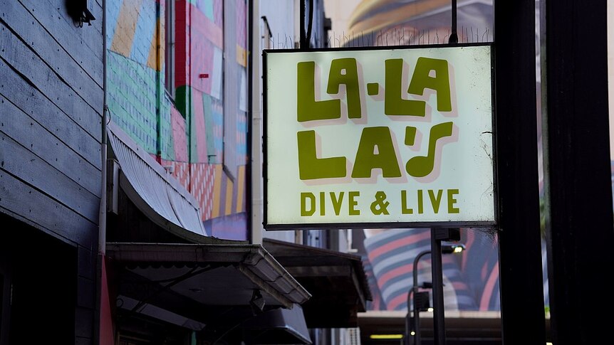 A bar sign that reads La la las hangs next to a coloured war and above the street