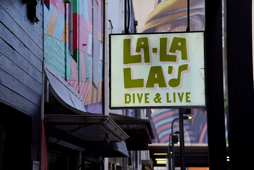 A bar sign that reads La la las hangs next to a coloured war and above the street