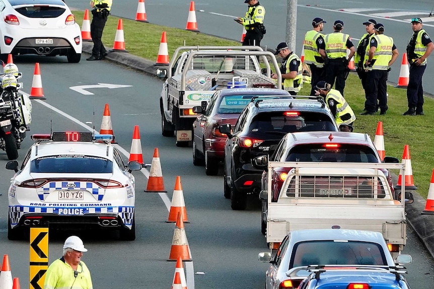 A line of vehicles waiting to be inspected by a group of police officers on a road.