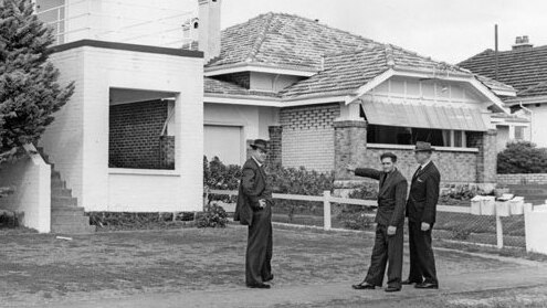 Black and white pic of serial killer Eric Edgar Cooke pointing with detectives outside a house.