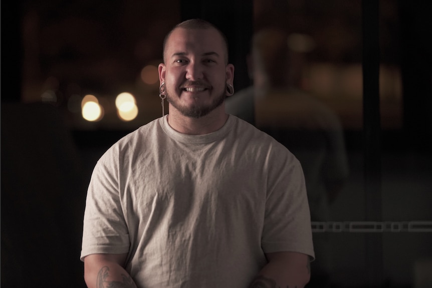 A man in a grey t-shirt smiles at the camera.