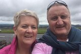 A middle-aged couple takes a selfie under a cloudy sky.