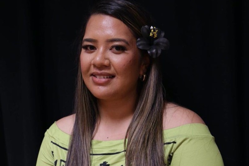A Samoan woman wears a flower on her ear in a green island dress
