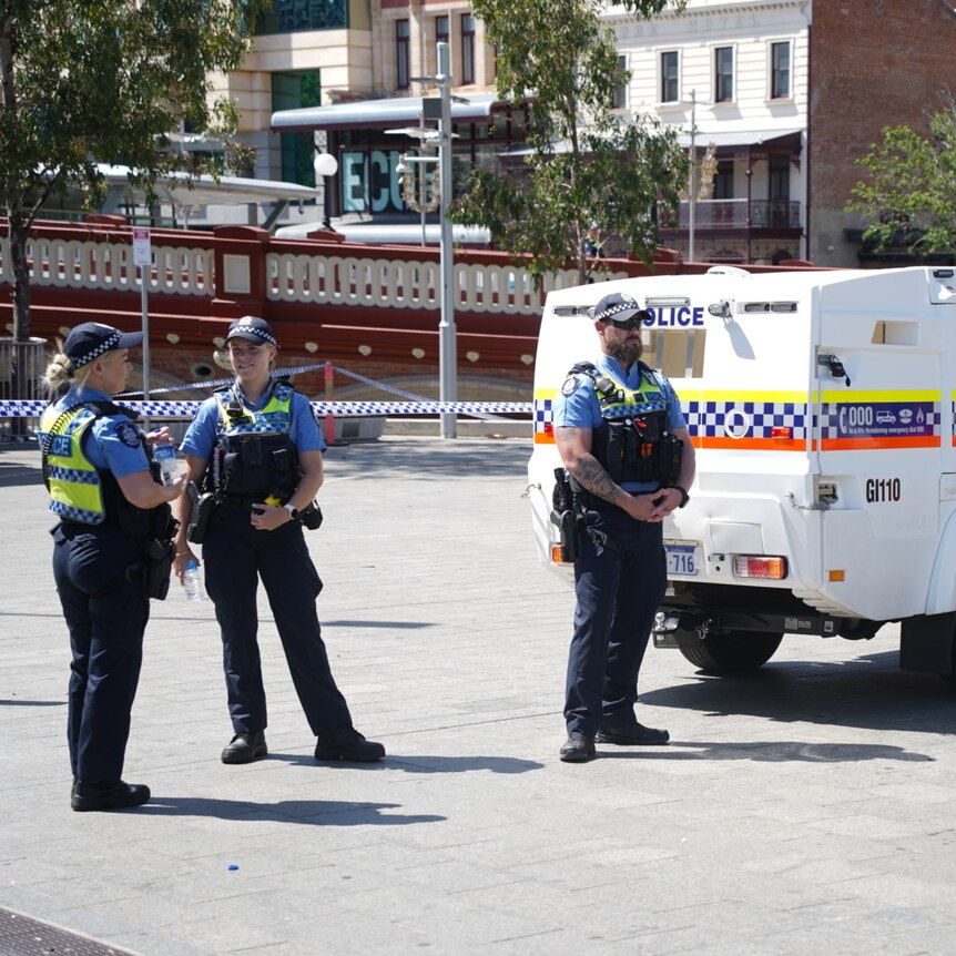 Three police officers stand next to a police vehicle in Yagan Square.