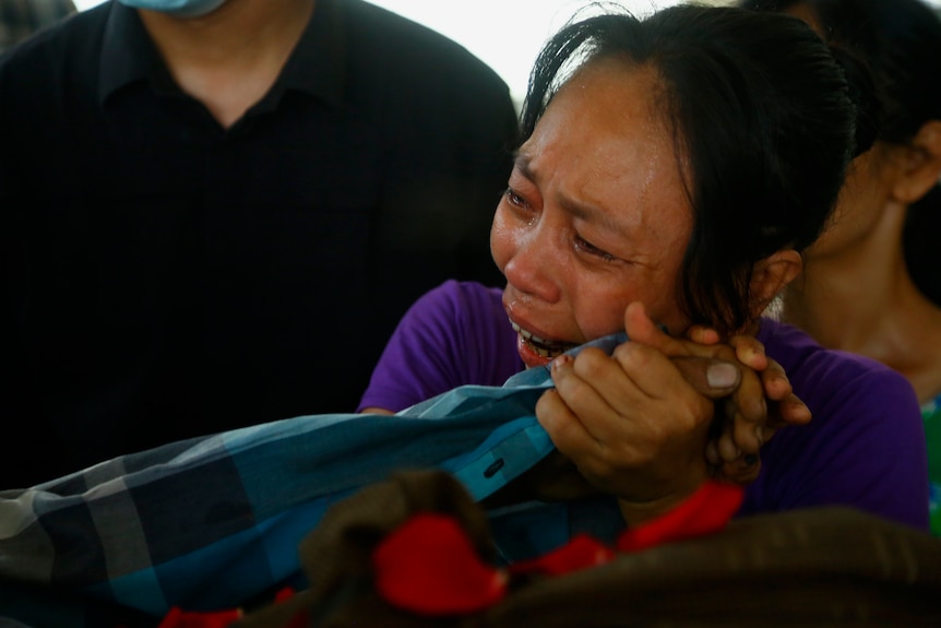 A family member cries as she holds the hand of a deceased loved one.