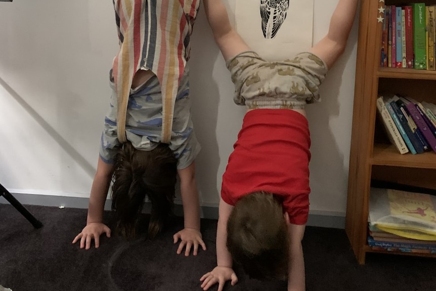 A mum and her son do a handstand against the wall of their home with their faces to the wall.