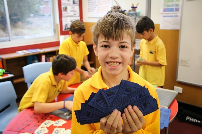 A student from Reservoir East Primary School holds up his class bank notes as part of a finance program.